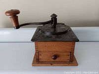 Front view of antique coffee grinder showing cast iron top with crank and pine wood base drawer