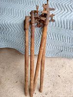 Full view of four antique clamps standing upright showing long oak handles and cast iron clamp heads with wing screws