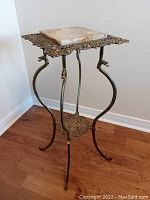 Full view of plant stand showing the curved legs, ornate openwork brass frame, and square marble insert on top.