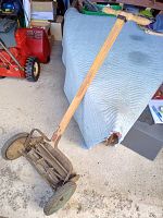 Full view of the Smarts antique push reel mower showing wooden handle, reel blade, and wheels on floor.