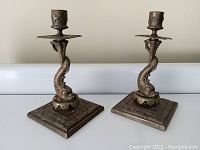 Pair of bronze dolphin form candlesticks on square bases, showing full view and relative height