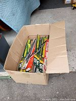 Cardboard box filled with multiple vintage wiper blades mostly in packaging with some loose blades.