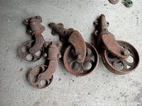 Five antique cast iron swivel caster wheels with rust and patina on concrete floor.