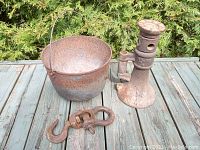 Photo shows three items: an antique screw type barn jack with visible thread and base, a cast iron bucket with holes for drainage and wire handle, and a cast iron hook and shackle.