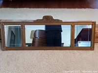 Front full view of the three panel gilt wood framed mirror resting on carpet.