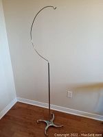 Full view of the tall, slender birdcage stand with curved hook top and four-legged base.