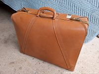 Closed view of the vintage tan leather suitcase showing overall exterior condition and handle wear.