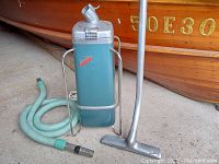 Full view of vintage teal-blue AirWay Sanitizor vacuum cleaner with green fabric hose and metal floor nozzle.