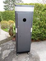Front view of tall metal radio equipment cabinet, dark gray with silver trim and circular cutout in door, showing the Motorola logo and locked door on wheels.