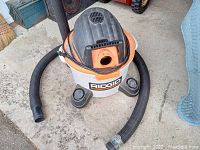 Top view of Ridgid shop vacuum showing white tank, orange/black top, hose detached and positioned beside it.