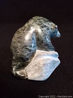 Side view of soapstone grizzly bear climbing a rock, showing the polished surface and texture of the carving.