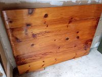 Photo showing the full varnished pine table top resting vertically against a wall with visible wood grain and knots.