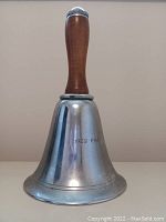Front view of the metal bell-shaped cocktail shaker with engraved dates and wooden handle.