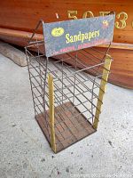 Full view of vintage 3M sandpaper display rack showing wireframe shelves and top labeled sign