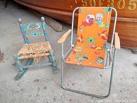 Photo showing the two chairs side by side on concrete floor, a blue wooden Mexican-style rocking chair with woven seat on left and folding chair with monkey fabric on right.