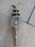 Single view of a copper and brass outdoor lantern with eagle finial on top, showing aged patina and glass panels.