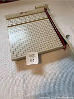 Top view of a rectangular metal paper cutter with grid lines, ruler edge, and BOSTON branding.
