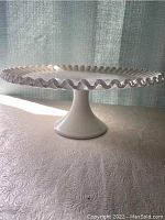 Side view of white cake dish showing ruffled edges and pedestal base