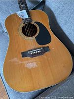 Full view of guitar body showing natural wood finish, black pickguard, and wear marks on the top.