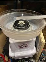 Full view of white cotton candy machine with clear plastic bowl and scoop on top.