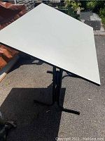 Full view of the drawing table tilted with black metal legs standing on pavement.
