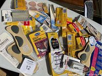 Overall view of the lot showing 25 plus new foot comfort products spread out on a white surface, including insoles, heel cushions, adhesive pads, foot sleeves, and laces.