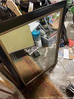 Full view of large rectangular mirror showing black frame with decorative inner trim and reflection of surrounding area.