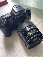 Front angle showing Minolta Maxxum film camera with attached Sigma 35-135mm zoom lens, displaying branding and lens aperture markings.