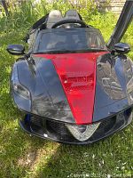 Front view of Moderno kids electric car showing black and red color scheme and sporty front grille.