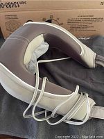 Full view of light brown and beige neck massager with padded and mesh interior and attached power cord.