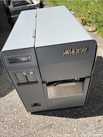 Front and side view of gray Sato label printer with control panel and button array showing model and brand details.