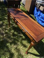Full view of the wooden side table on grass showing tabletop and drawers