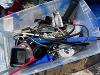 Plastic bin with assorted cables, cords, hoses, a gray container, and a push broom handle.