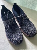 Pair of black and white speckled athletic shoes with laces, showing overall condition and design detail