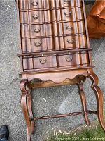 Photo of the entire wooden bar cabinet showing curved legs, multiple small drawers with brass handles, and pull-out table drawer.