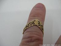 Ring shown on finger displaying size and fit. Highlights pierced design and chevron-shaped solid top section.