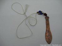 Full view of necklace showing wooden paddle pendant with copper face and string of old beads on white cord.