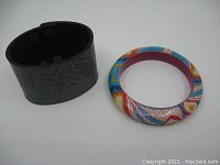 Two bracelets: colorful indigenous painted bangle and black leather embossed wrist band.