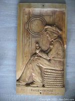 Full view of the hand carved wood panel showing a seated figure and porthole, with inscription and artist signature at base.