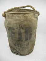 Overall front view of the stained and worn canvas fire bucket with rope handle and stamped 'FAB' lettering.