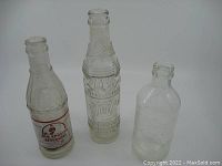 Three vintage glass pop bottles shown together, identifying shapes and embossing clearly visible.