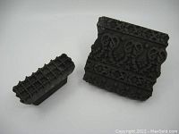 Two antique hand carved wooden fabric stamps, one large with intricate floral pattern and one smaller with grid pattern, shown together on white background.