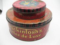 Side view of two stacked Mackintosh's candy tins showing overall decoration and wear.