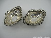Top-down view of two sterling silver pierced bon bon dishes showing floral pierced patterns inside bowl area and decorative embossed rim.