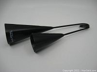 Black metal Tycoon Percussion agogo bell showing the two connected conical bells and curled handle end from an angle, painted black.