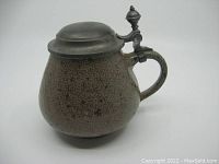 View of the stein angled to show the handle and pewter lid with thumb lift finial against white background.