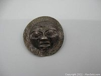 Front view of round sterling silver brooch/pendant with a cast indigenous face and textured background.