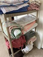 Four-shelf plastic shelving unit holding multiple bedding items, including quilts, blankets, and comforters in various colors and folded styles.