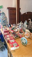 Overview of Christmas decorations arranged on a wooden table including snowmen figurines, snowglobes, collectibles, and boxes of ornaments.