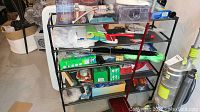 Front view of black metal shelving unit filled with cleaning products and tools including sprays, boxes, and cleaning tools.